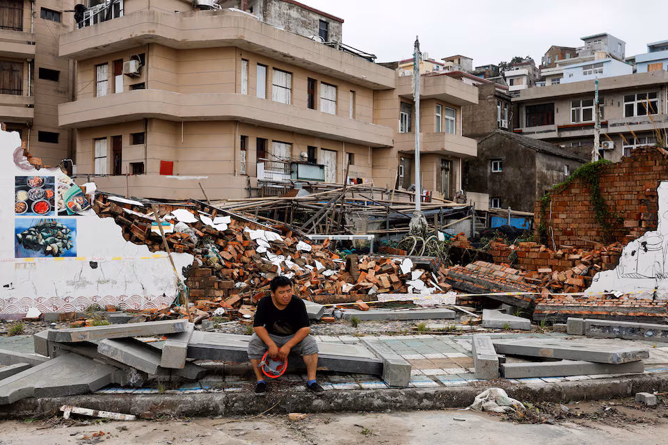 A person sits beside a collapsed wall in the aftermath of Typhoon Bavi in the coastal village of Dongsha, Taizhou, Zhejiang province